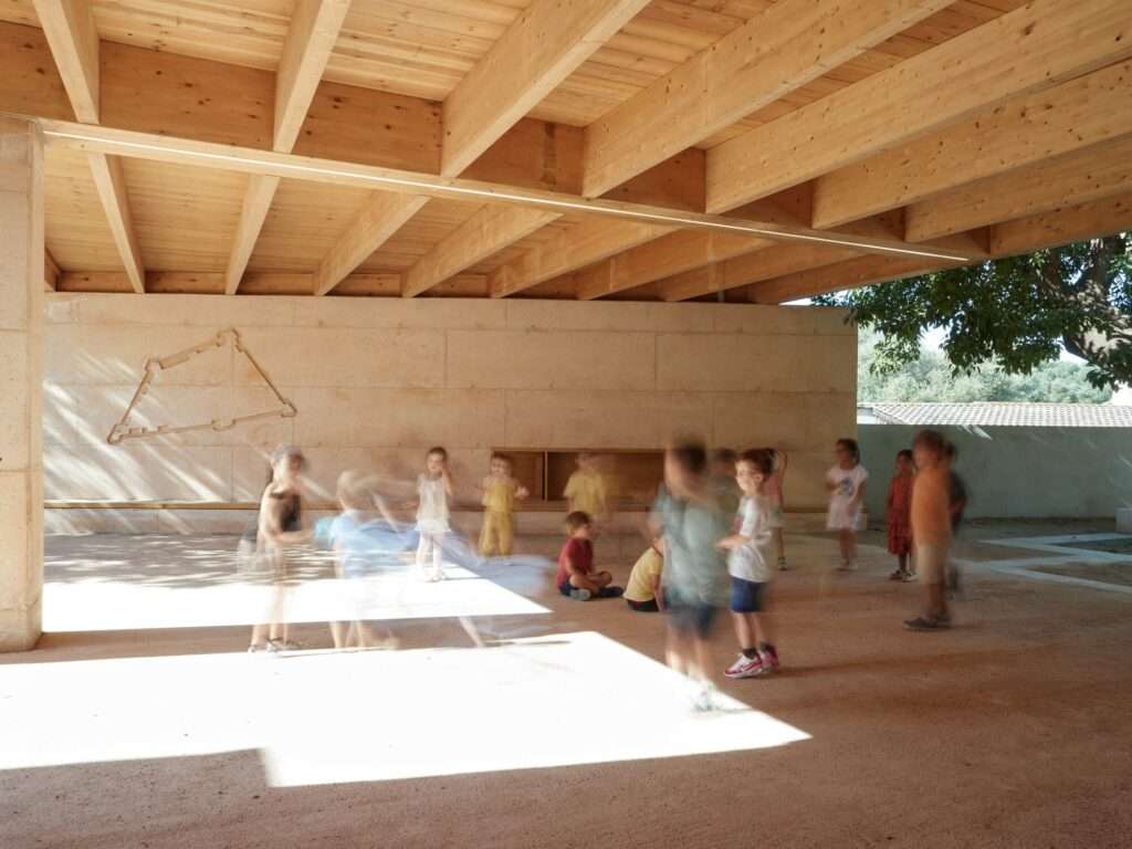 A group of elementary children playing in motion blur inside a shaded courtyard with an engraved historical fortress map on a concrete wall.