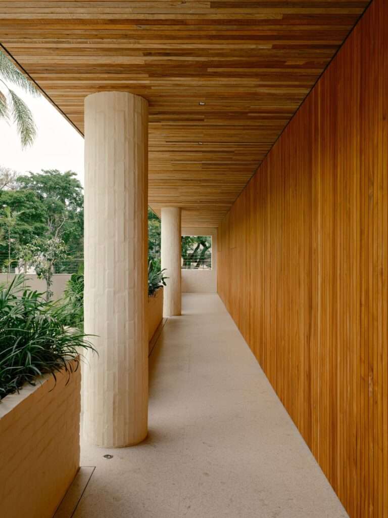 Perspective view of an outdoor portico hallway with vertically stacked brick columns, a wood slat ceiling, a wood-clad wall, and built-in planters.