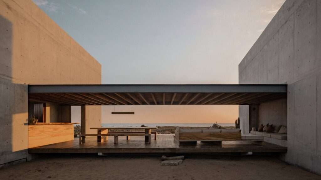 Open-air covered timber deck with dining table and seating overlooking the ocean through concrete wall framing.
