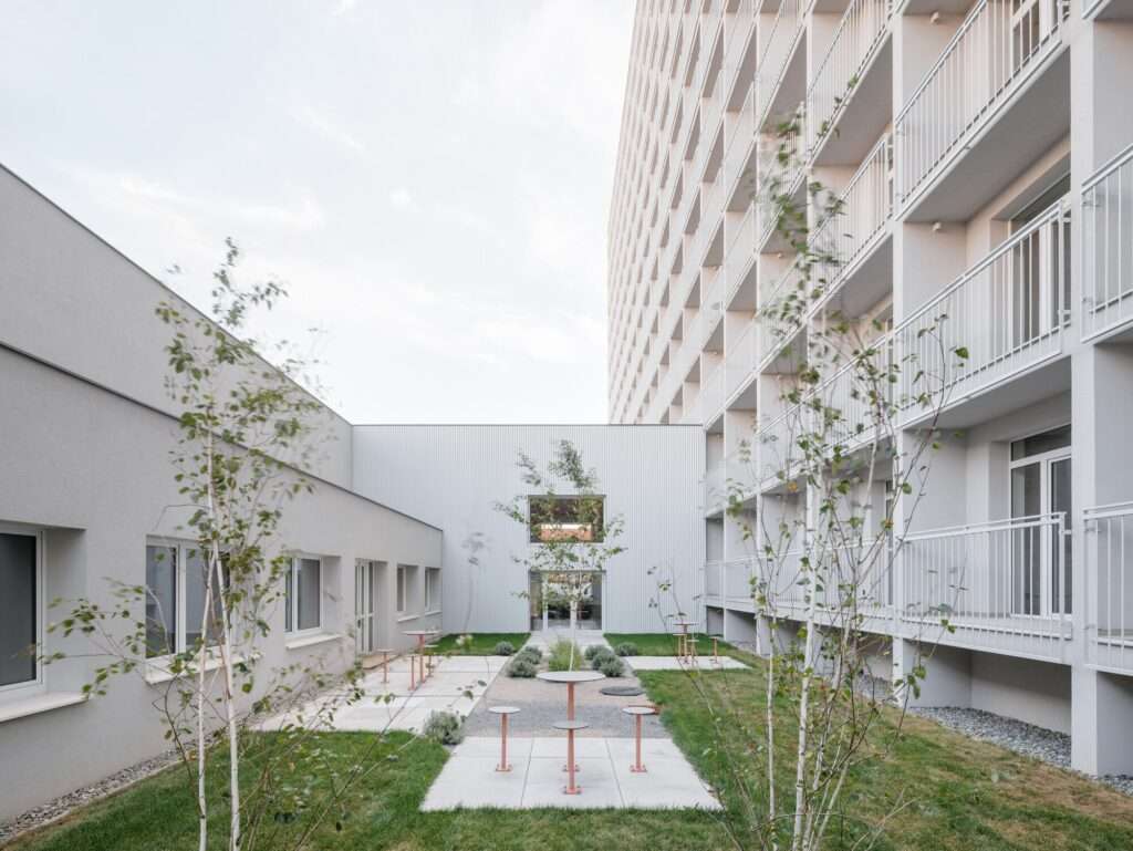 Minimalist white interior courtyard of Terasa residential complex featuring small trees, paved seating areas, and rows of private balconies.