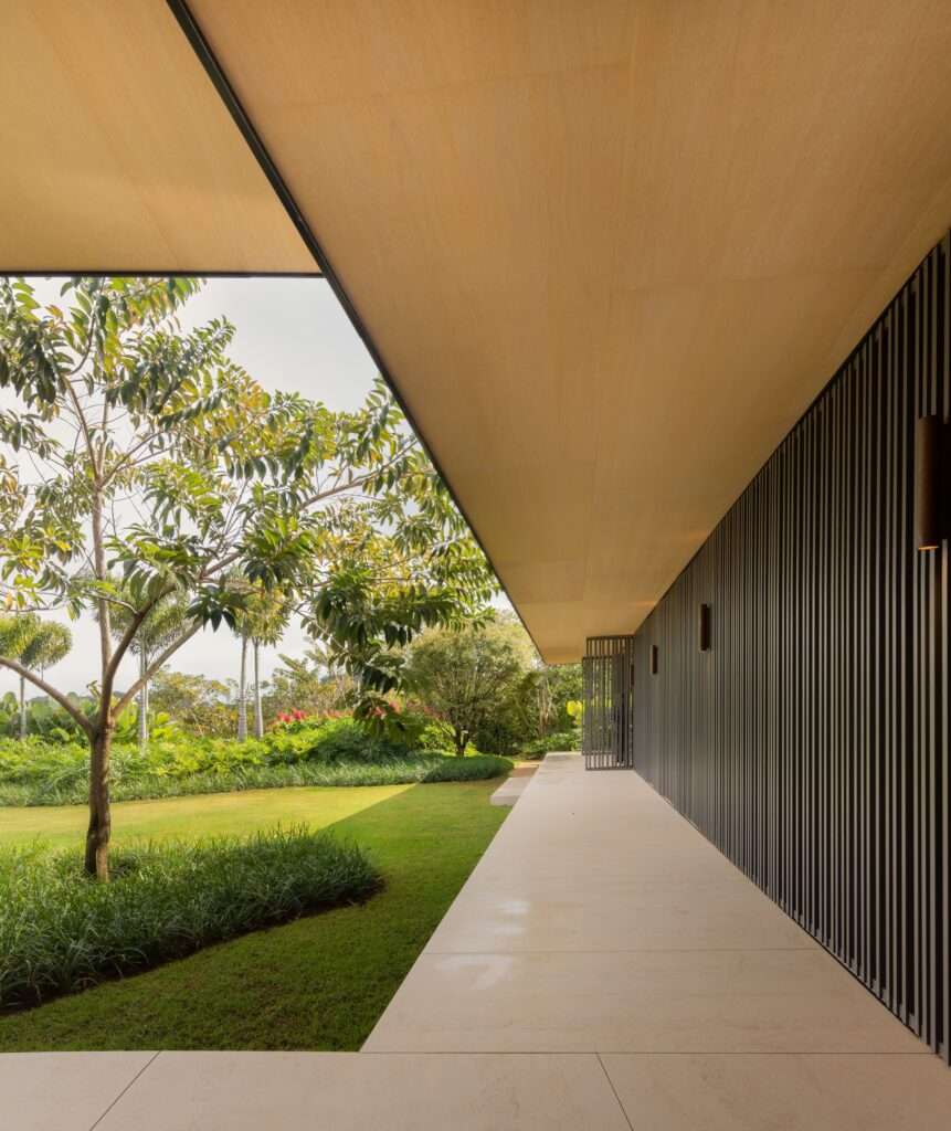 A long shaded outdoor corridor alongside a dark vertical slatted brise-soleil facade under a wide wooden soffit.