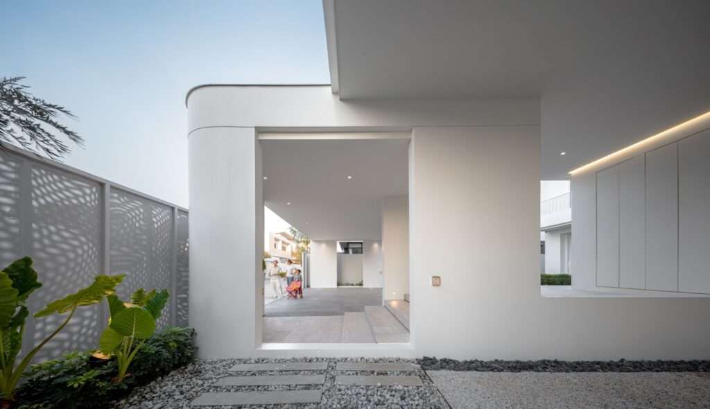 Architectural threshold at JNG House looking through a large rectangular wall opening toward the carport and entry stairs, flanked by gravel paths.