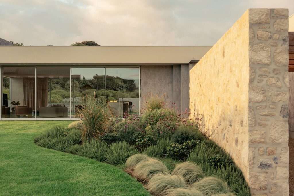 Reclaimed stone wall surrounded by native coastal plantings and manicured grass next to the glass facade of Wildcoast House.