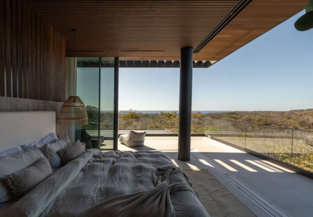 Modern luxury bedroom with floor-to-ceiling glass doors opening to a private terrace with ocean views at KUL Nosara.