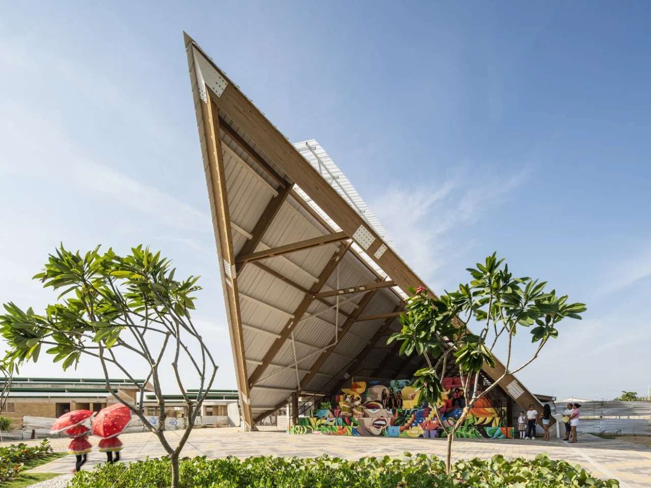 Dramatic pointed timber and steel roof canopy of Vilas de San Pablo Cultural Center with a colorful community mural underneath.