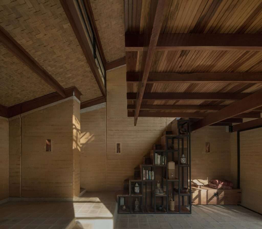 Close-up of a custom-designed, multi-functional staircase and shelving unit made of metal and wood, set against a textured rammed earth wall.