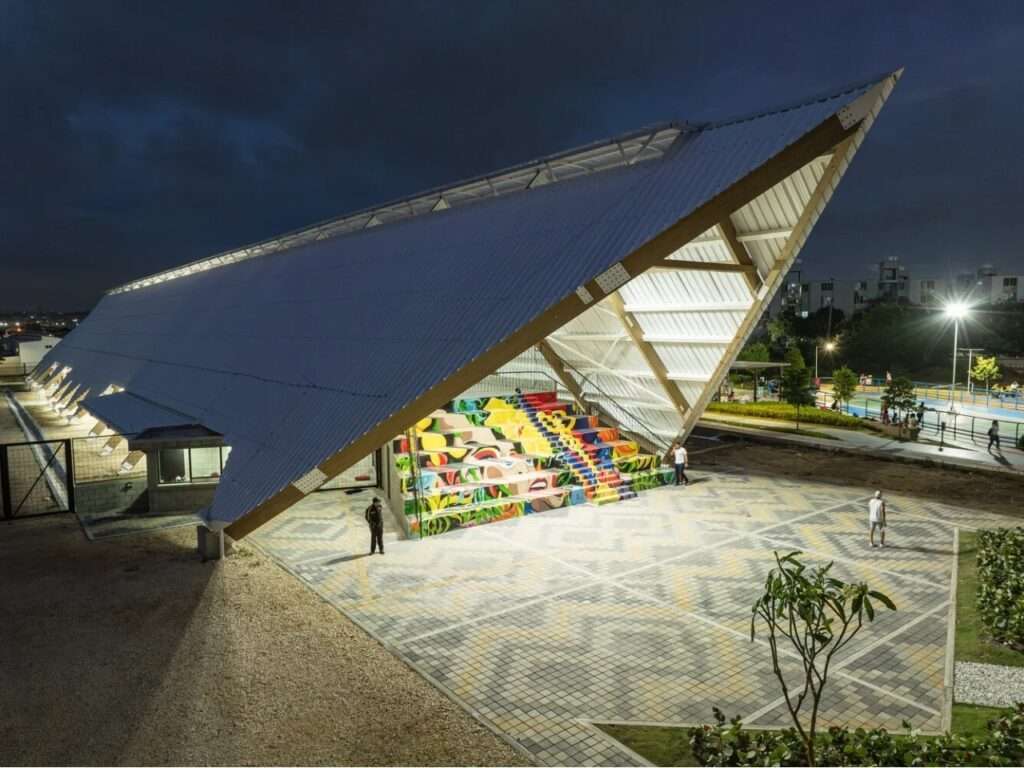 Dusk view of the illuminated Vilas de San Pablo Cultural Center showing the geometric paved plaza and colorful amphitheater seating.