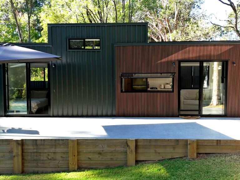 Exterior view of the Burley 9.6 tiny home showcasing a mix of dark vertical corrugated metal siding and warm NewTechWood slatted timber cladding next to a concrete patio.