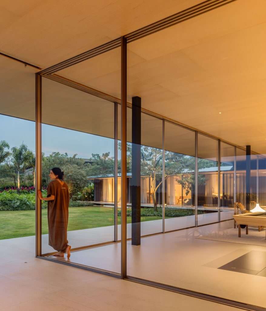 Night view looking through large corner glass sliding doors revealing an illuminated interior living area and a resident standing near the frame.