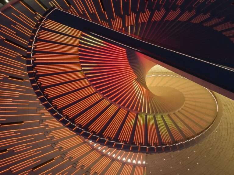Detailed view of the illuminated spiral staircase in the Shanghai Grand Opera House with red and orange linear LED lighting.