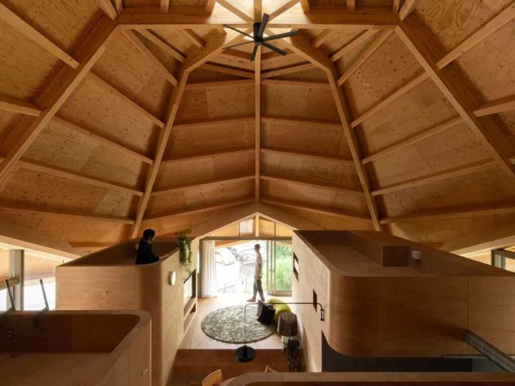 High-angle interior shot of a Japanese residential home showing an open-plan layout under a massive, geometric, eight-sided exposed timber roof structure.