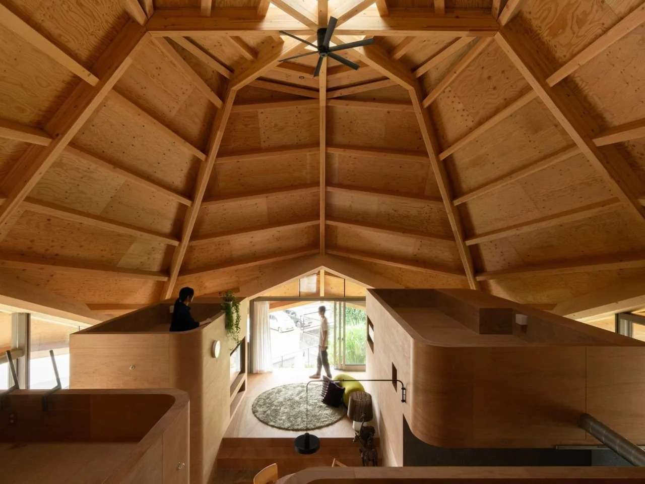 High-angle interior shot of a Japanese residential home showing an open-plan layout under a massive, geometric, eight-sided exposed timber roof structure.