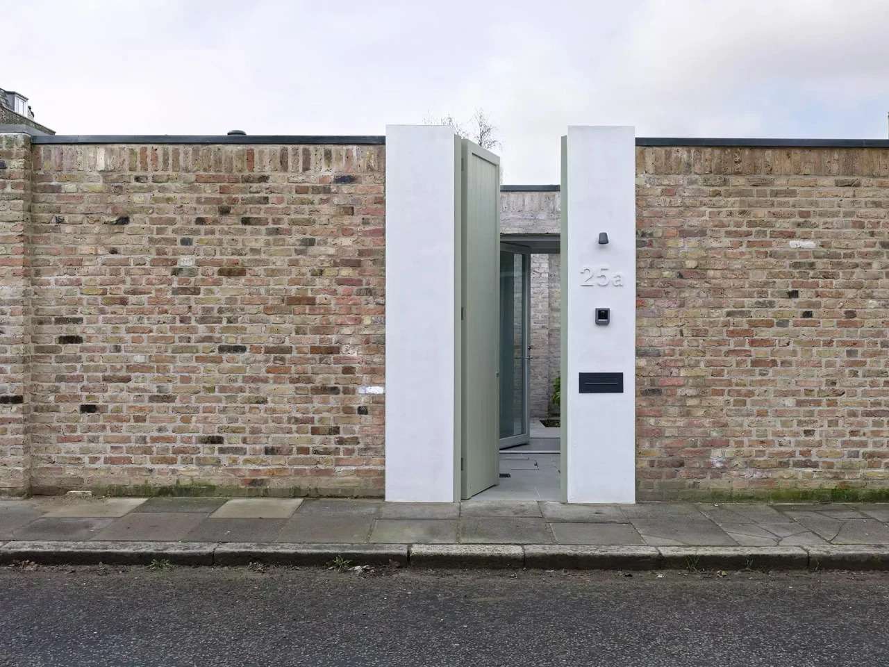 Reclaimed brick perimeter wall with a modern white concrete entrance and light green wooden door at Walled Courtyard House.