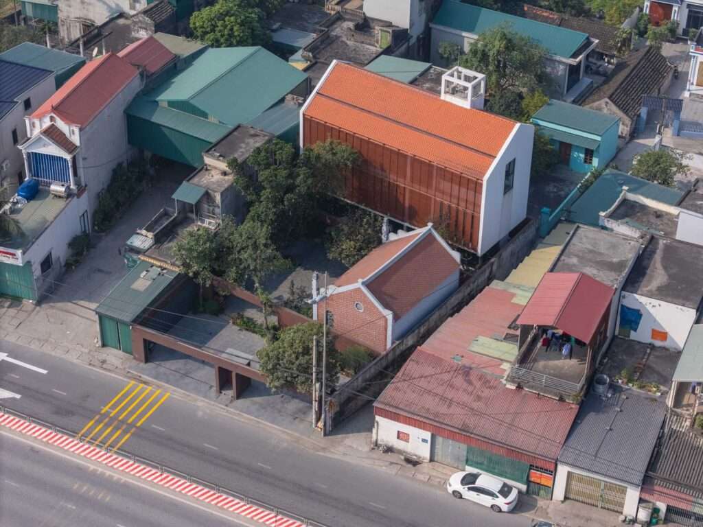 Aerial drone view of NB01 House showing its location next to a busy multi-lane national highway and surrounding urban fabric.