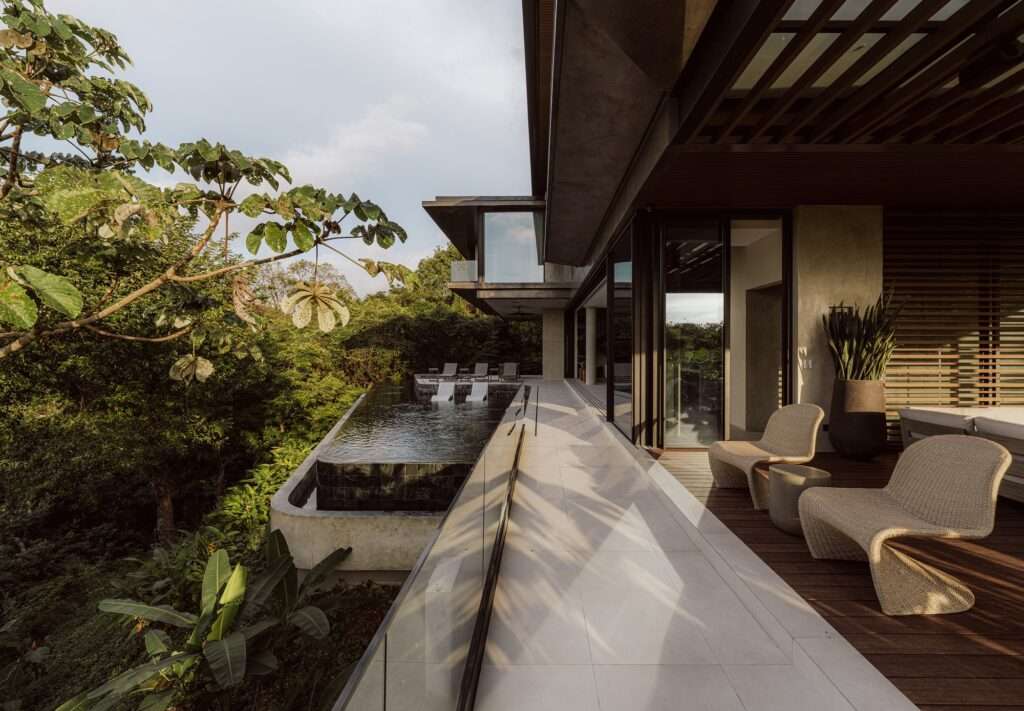 Covered exterior terrace featuring woven loungers and a cantilevered infinity pool integrated into the hillside trees at KUL Nosara.