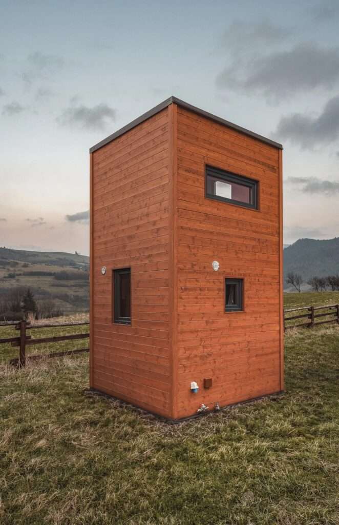 Low-angle exterior shot of La Ruche tiny home showing its treated pine wood facade and small rectangular windows against a cloudy sky.