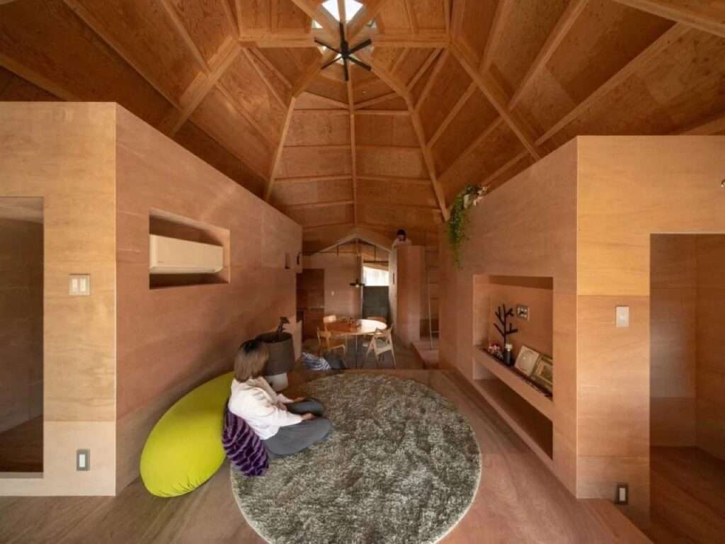 Ground level perspective of a sunken living room featuring a round rug, surrounded by functional plywood structure boxes under an octagonal wooden ceiling.