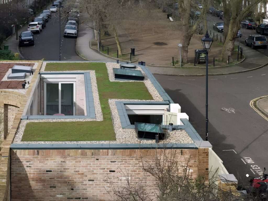 Aerial view of a flat sedum green roof with integrated skylights and courtyard cutouts on a contemporary brick house.