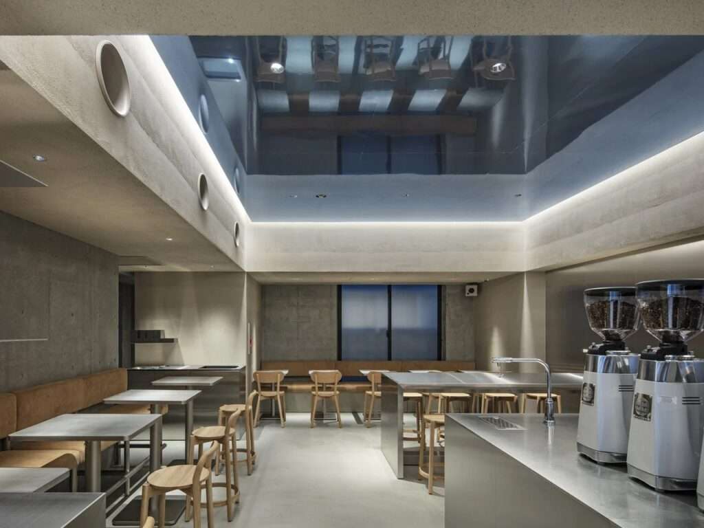 Full interior perspective of Blue Bottle Coffee Harajuku showing concrete walls, minimalist seating arrangements, and coffee grinding stations.
