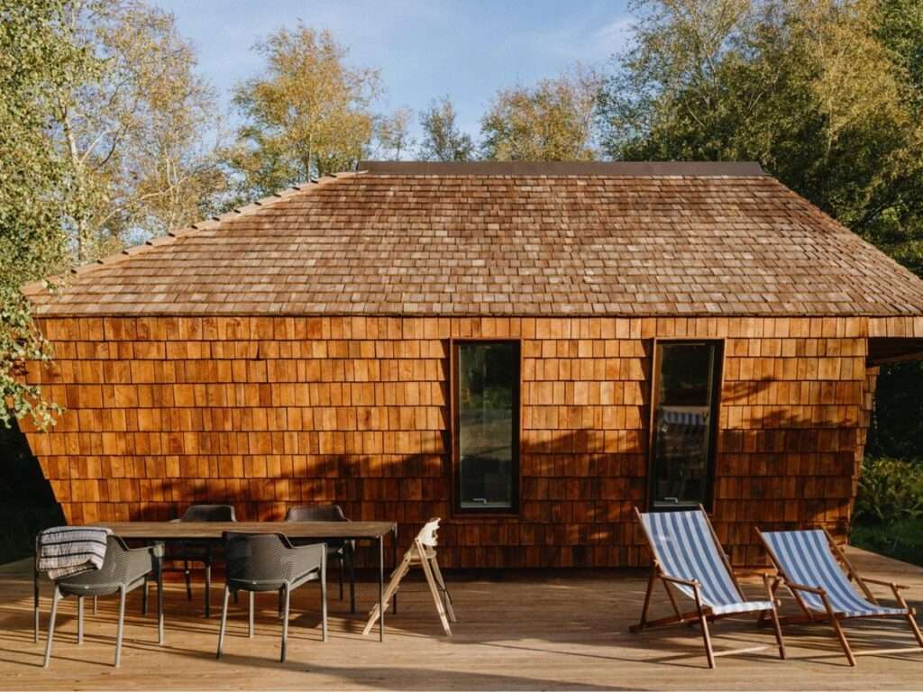 Side view of EcoNeo timber cabin with outdoor wooden deck, dining table, and lounge chairs.