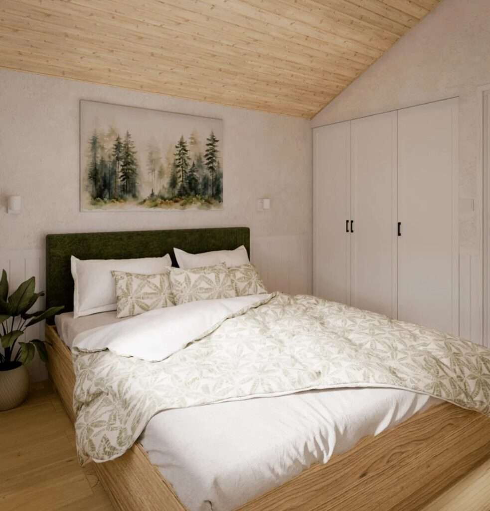 View of the master bedroom in the Vagabond Haven Evergreen XL, featuring a wooden double bed with a green moss-like headboard, a large built-in white wardrobe, and a nature-themed painting under a pitched wood ceiling.