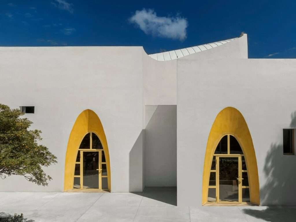 Close-up of two symmetrical golden arched doorways set in a smooth white concrete facade of the Santa Barbara Parish Complex.
