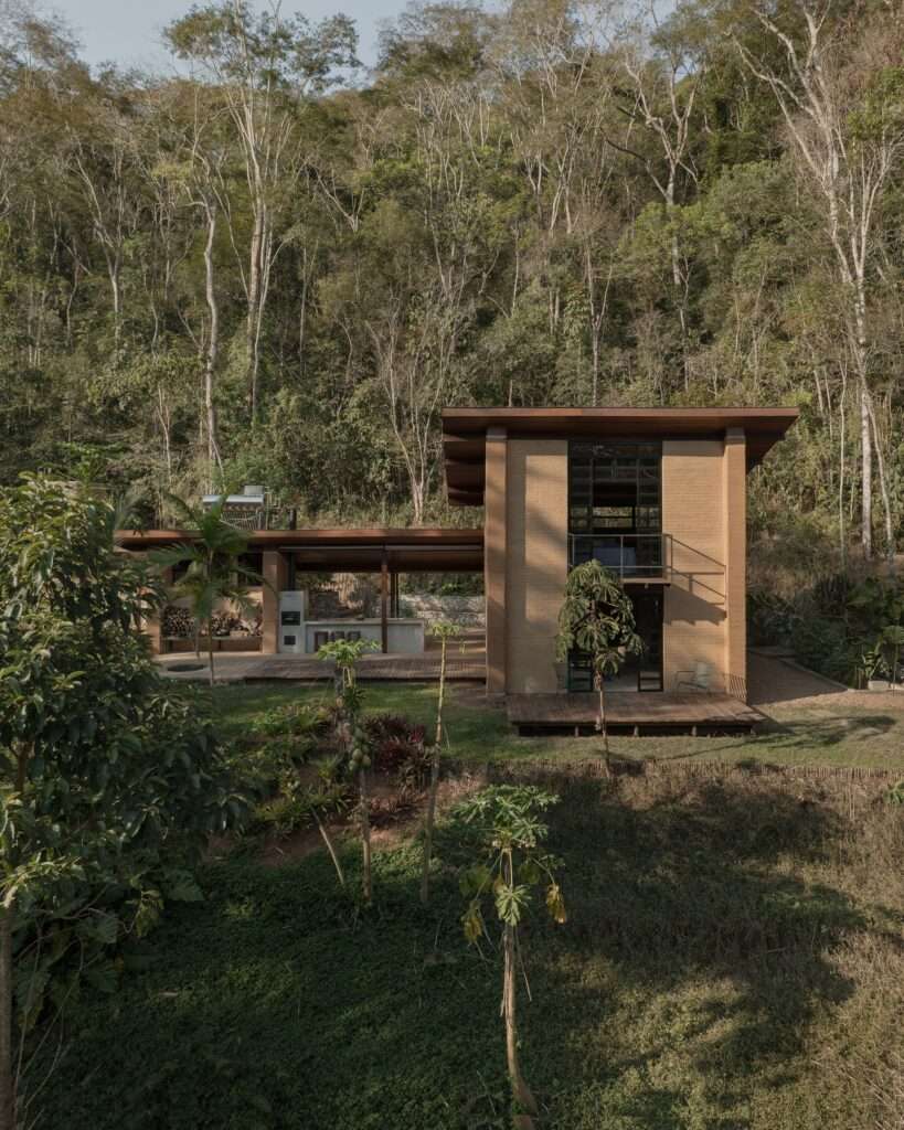 An elevated exterior view of the Lake Cabin, showing its two volumes nestled into the hillside among trees and native vegetation.