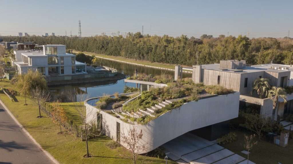 An elevated aerial drone photograph showing the spiral layout of a modern residence with extensive green roofs, situated along a linear water canal.