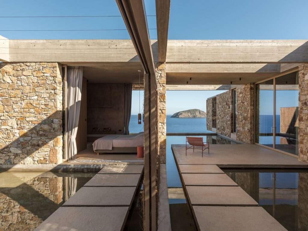 Interior-exterior transition space with stone walls, water elements, and a view of the Aegean Sea.