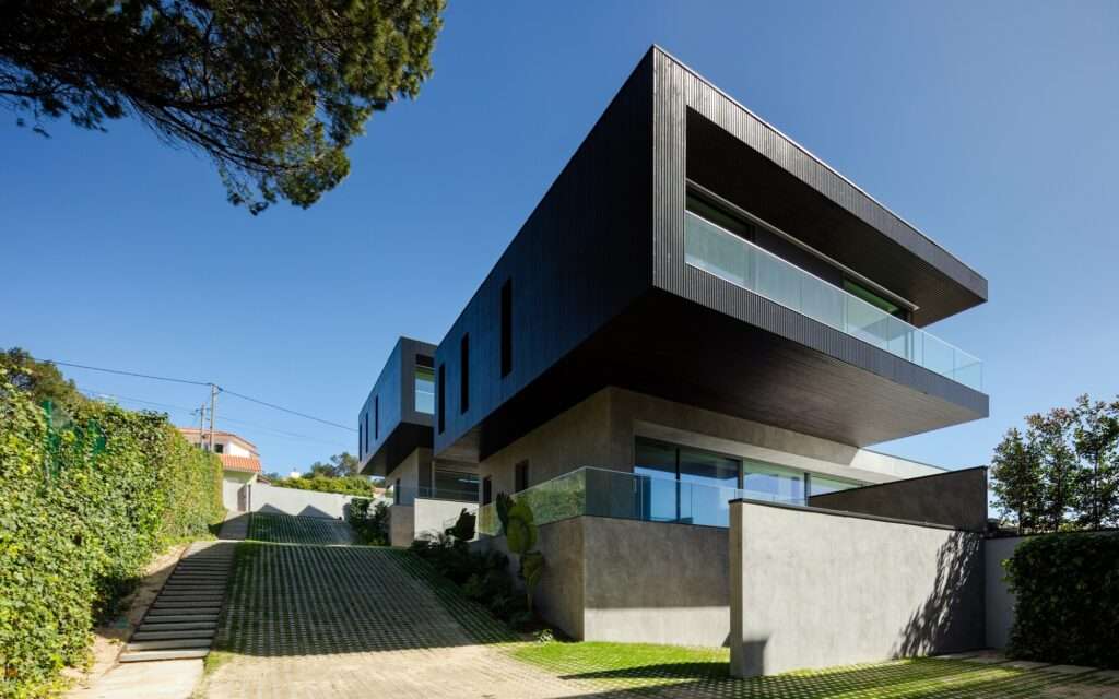 Daytime shot of a modern swimming pool with green tiled finishes on a stone terrace, reflecting the dark wood and glass facade of the residence.