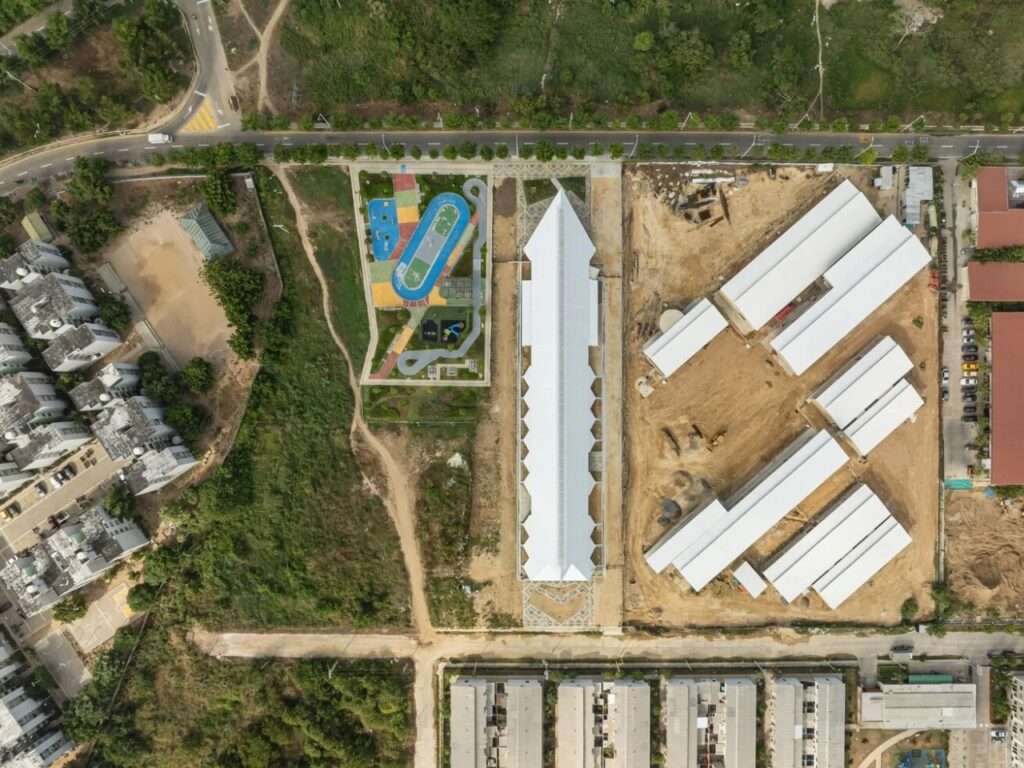 Direct top-down drone view of the linear white roof structure of Vilas de San Pablo Cultural Center next to a colorful park.