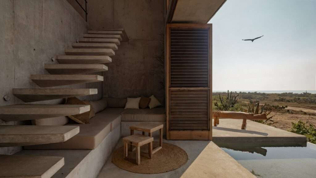 Floating cantilevered concrete staircase inside a minimalist room with built-in lounge seating and open views to the outdoors.