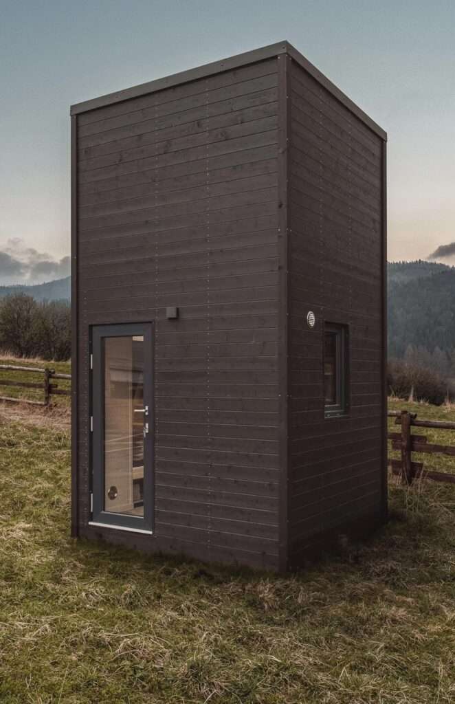 Dark stained exterior wood siding of La Ruche house featuring the glass entrance door at the ground level.