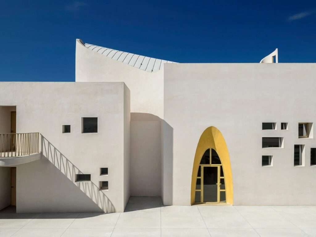 Clean geometric facade of Santa Barbara Parish featuring a single golden arched door, square windows, and sharp shadows.