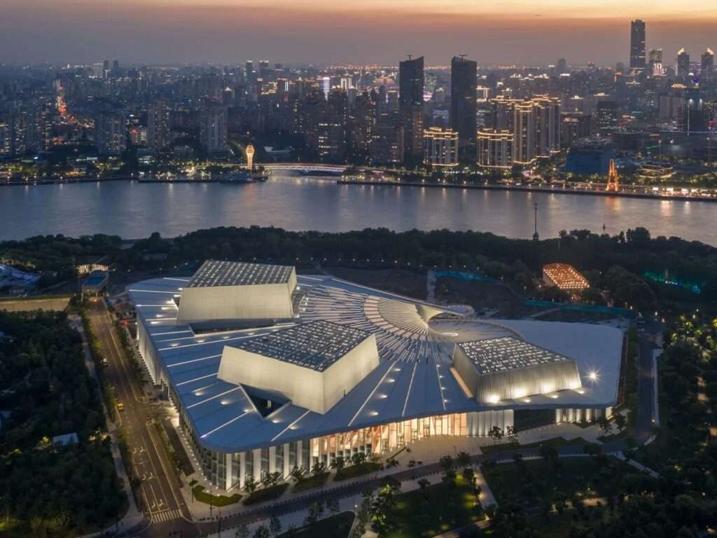 Aerial sunset view of the Shanghai Grand Opera House on the banks of the Huangpu River with city skyline.