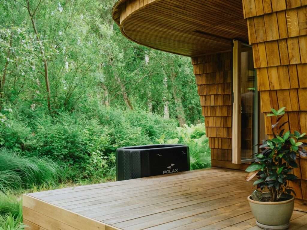 Close up of EcoNeo cabin wooden deck corner with a plunge tub overlooking a dense green forest.