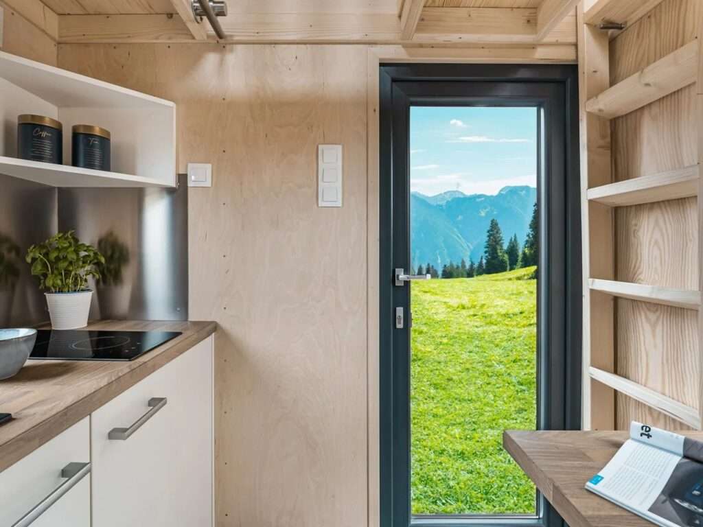 Interior view of La Ruche kitchen looking through an open glass door out to a vibrant green alpine mountain landscape.