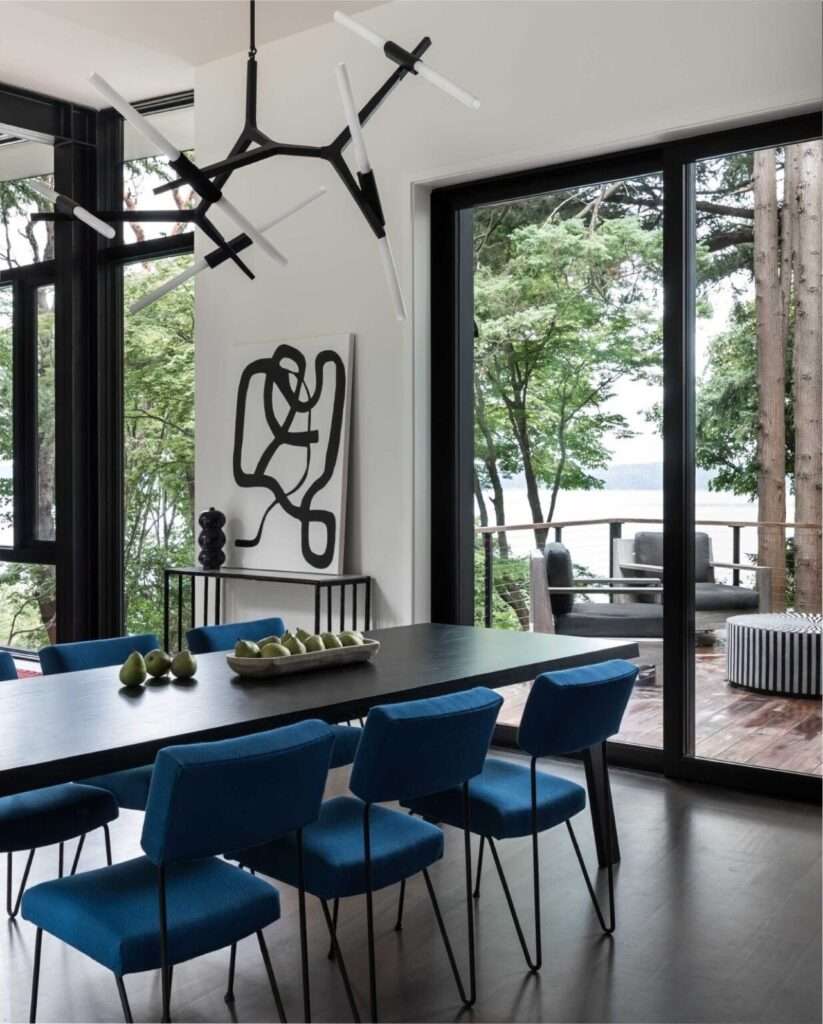 Contemporary dining area with a black table and blue chairs looking out through sliding glass doors to a forested terrace and water view.