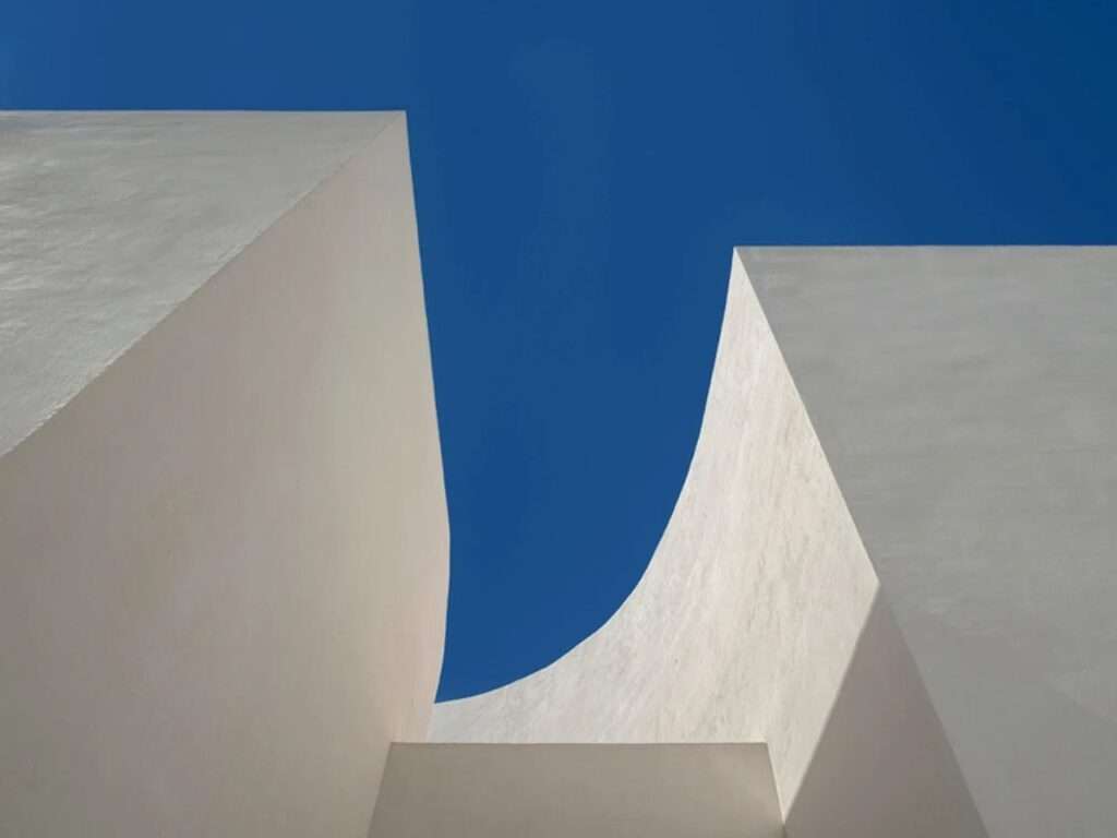 Abstract architectural upward view of two curving white concrete walls of Santa Barbara Parish meeting against a deep blue sky.