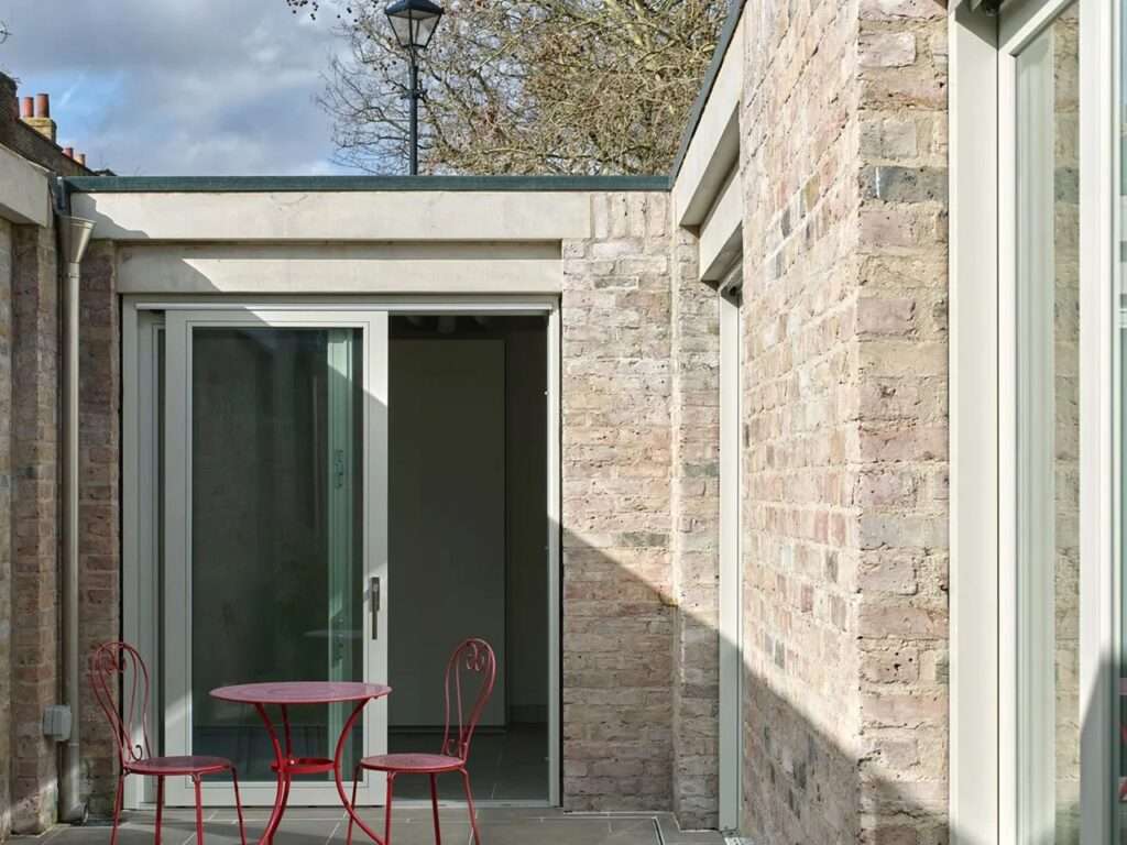 Minimalist red metal patio table and chairs sitting in a courtyard next to a lime-mortared brick wall.