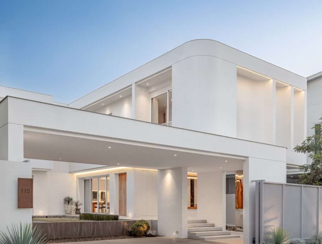 Low angle view of JNG House facade at twilight featuring illuminated steps leading up to the main door beneath a cantilevered white upper volume.