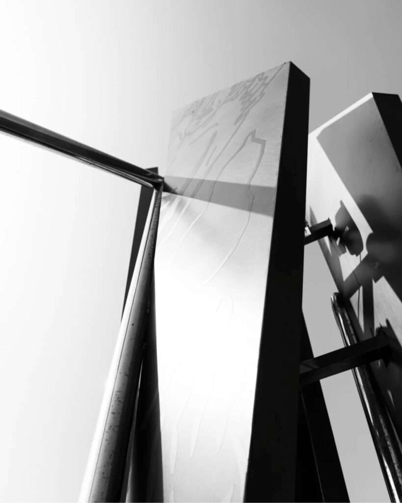 High-contrast black and white close-up of a sharp metallic column and its shadow cast on the structure.