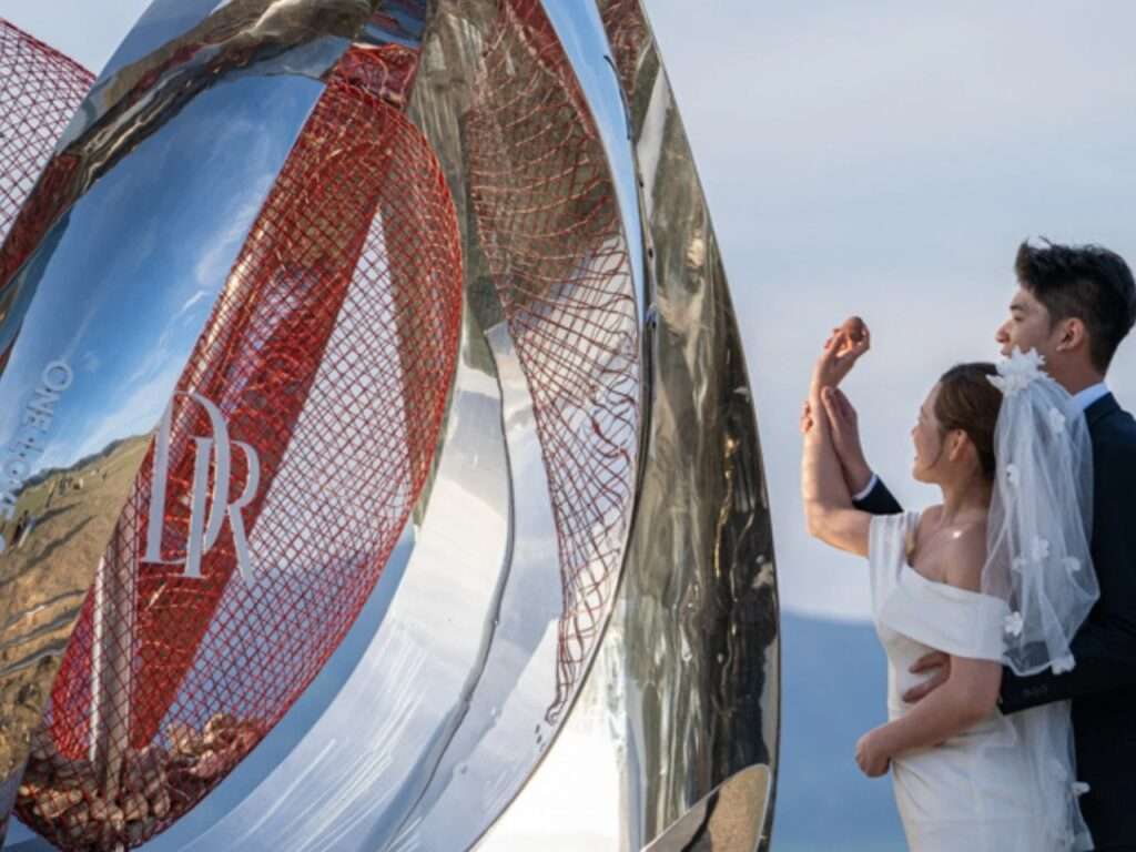 A bride and groom interact with the pavilion's red mesh cavity, placing small stones collected from around Sayram Lake inside the designated slots.