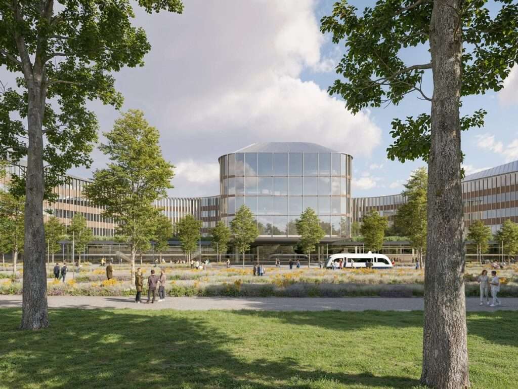 Central glass pavilion of Brescia hospital seen from an open wildflower meadow and pedestrian green park.