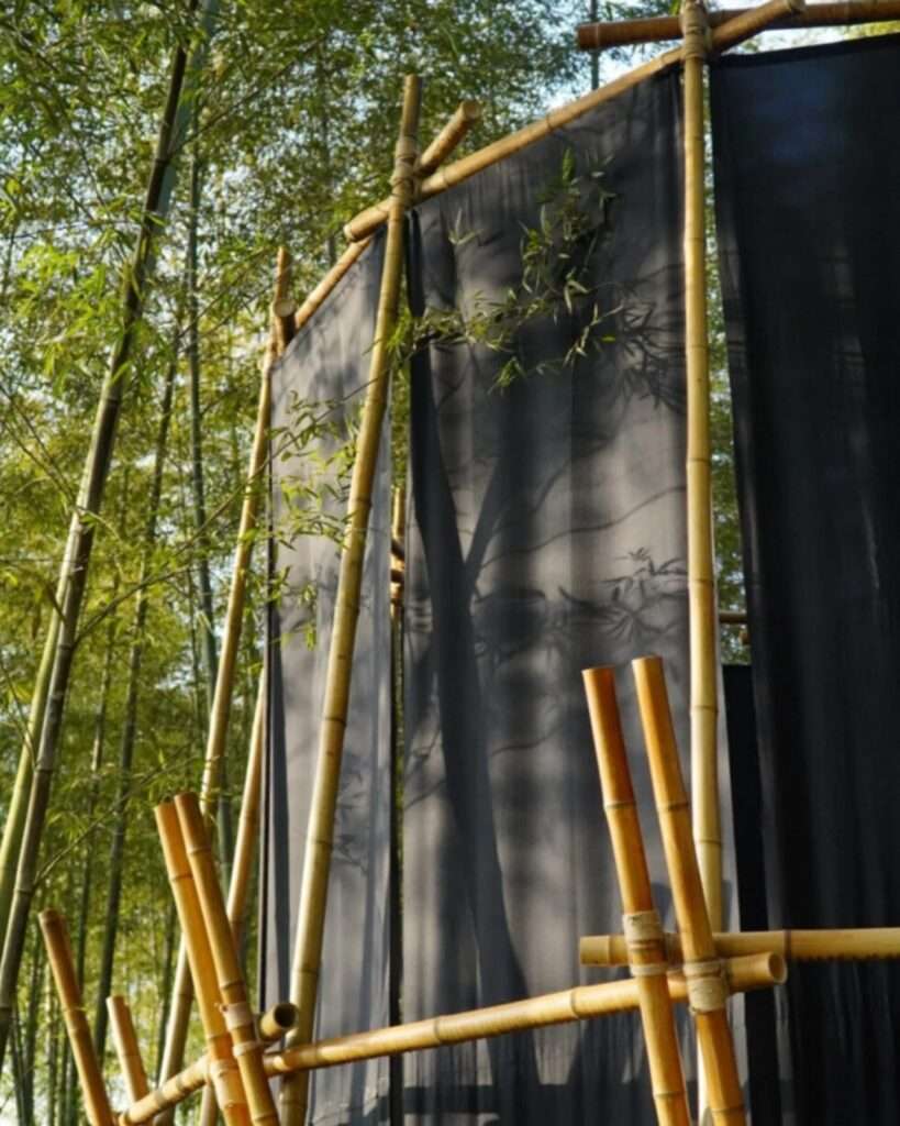 Sunlight casting sharp silhouettes and shadows of bamboo leaves and branches onto a semi-transparent dark linen-cotton fabric sheet.