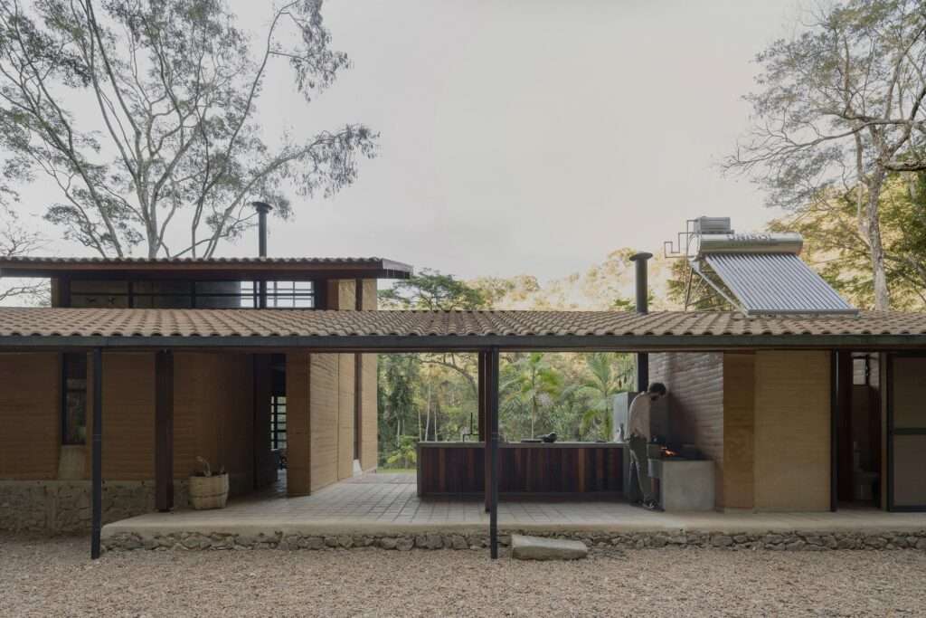 A covered outdoor kitchen and social area featuring a concrete counter, wood grill, and a solar thermal panel mounted on a tiled roof section.