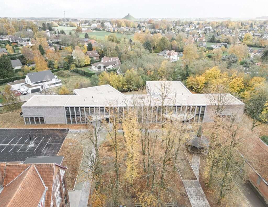 Aerial view of the Cardinal Mercier College modern expansion building with a branched layout amidst a wooded site and residential area.