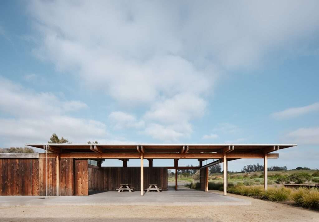 Side view of the open-air Live Oak Farm Pavilion with wooden picnic tables under a broad cantilevered roof canopy.