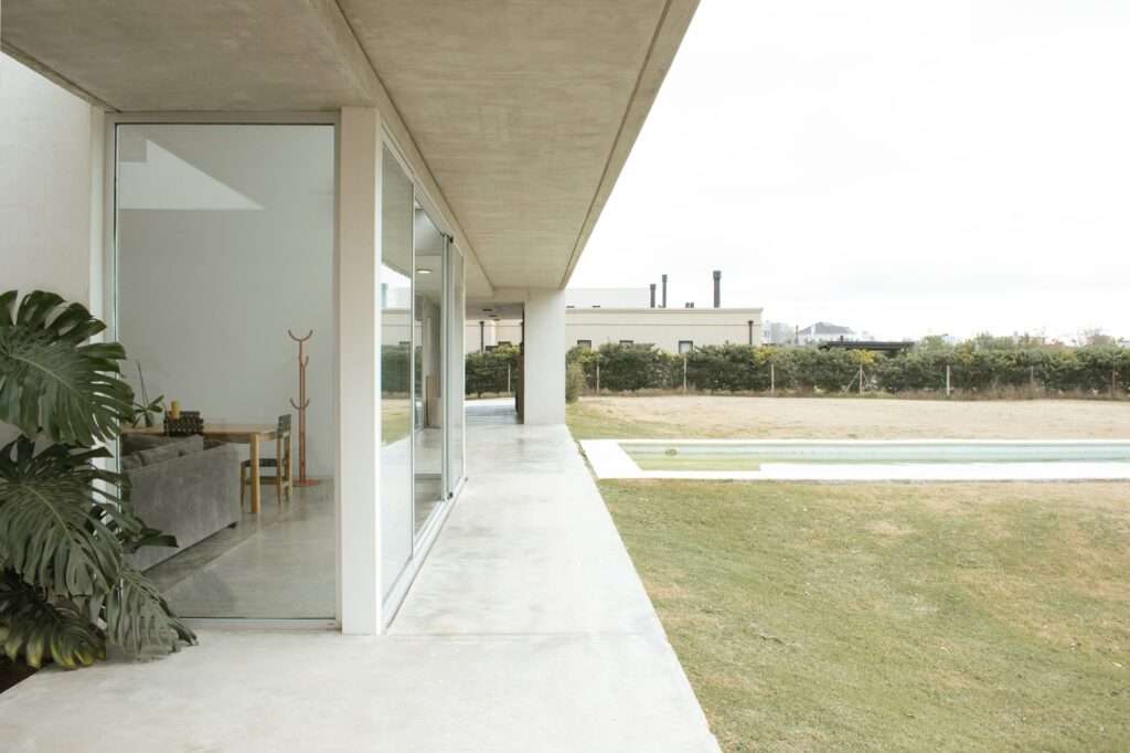 Casa O Dining Area with Large Glass Doors Opening to the Pool and Garden under a Concrete Beam.