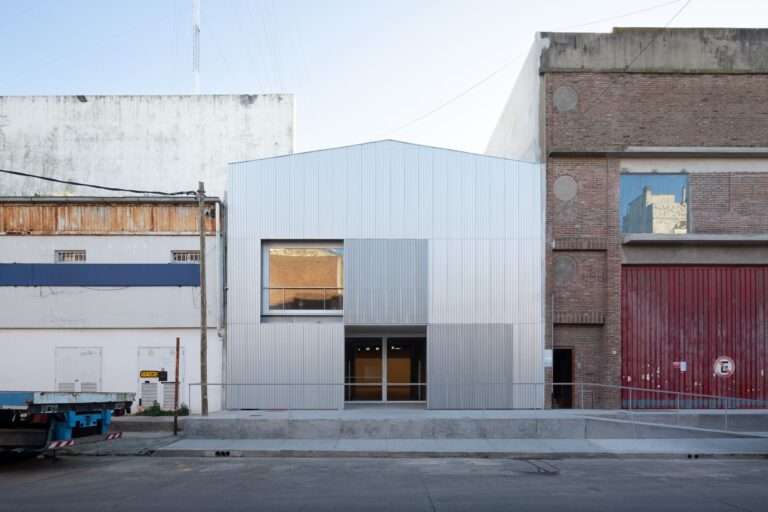 Modern industrial facade of the Larivière Foundation made of folded anodized aluminum panels under a gabled roof, nestled between old brick and concrete warehouse buildings in La Boca.